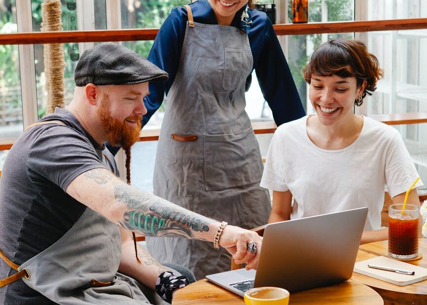 smiling multiracial cafe employees sharing laptop at work